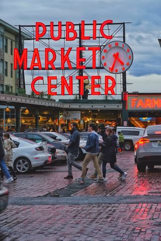 Pedestrians crossing wet cobblestones under the Public Market Center sign in the rain, Seattle