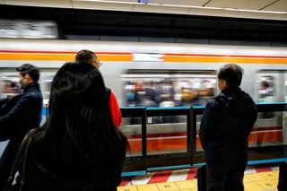Commuters waiting on a Tokyo Metro platform as a train blurs past